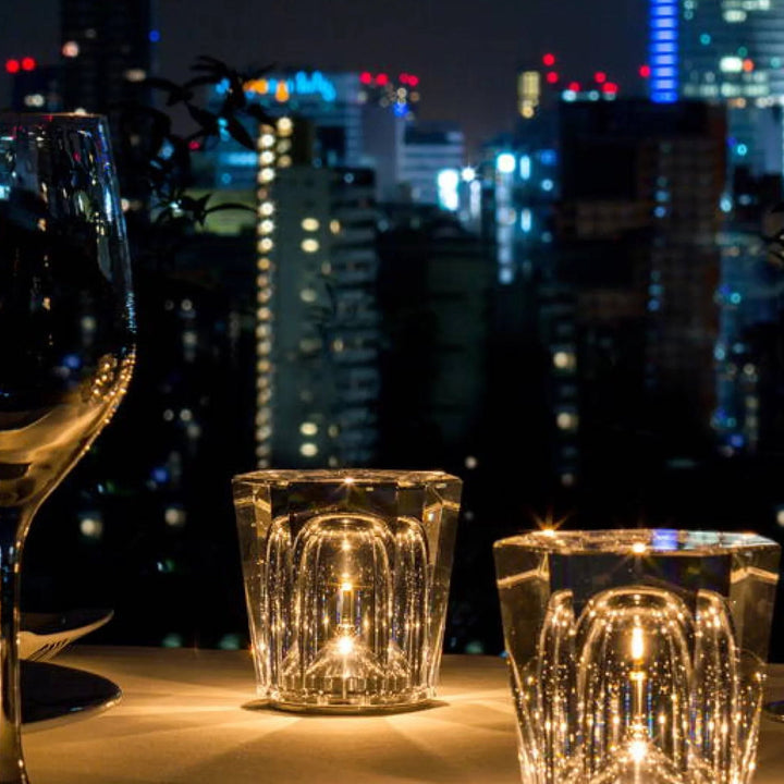 Gold transparent crystal table lamp, another view, glowing beside a wine glass on a table.