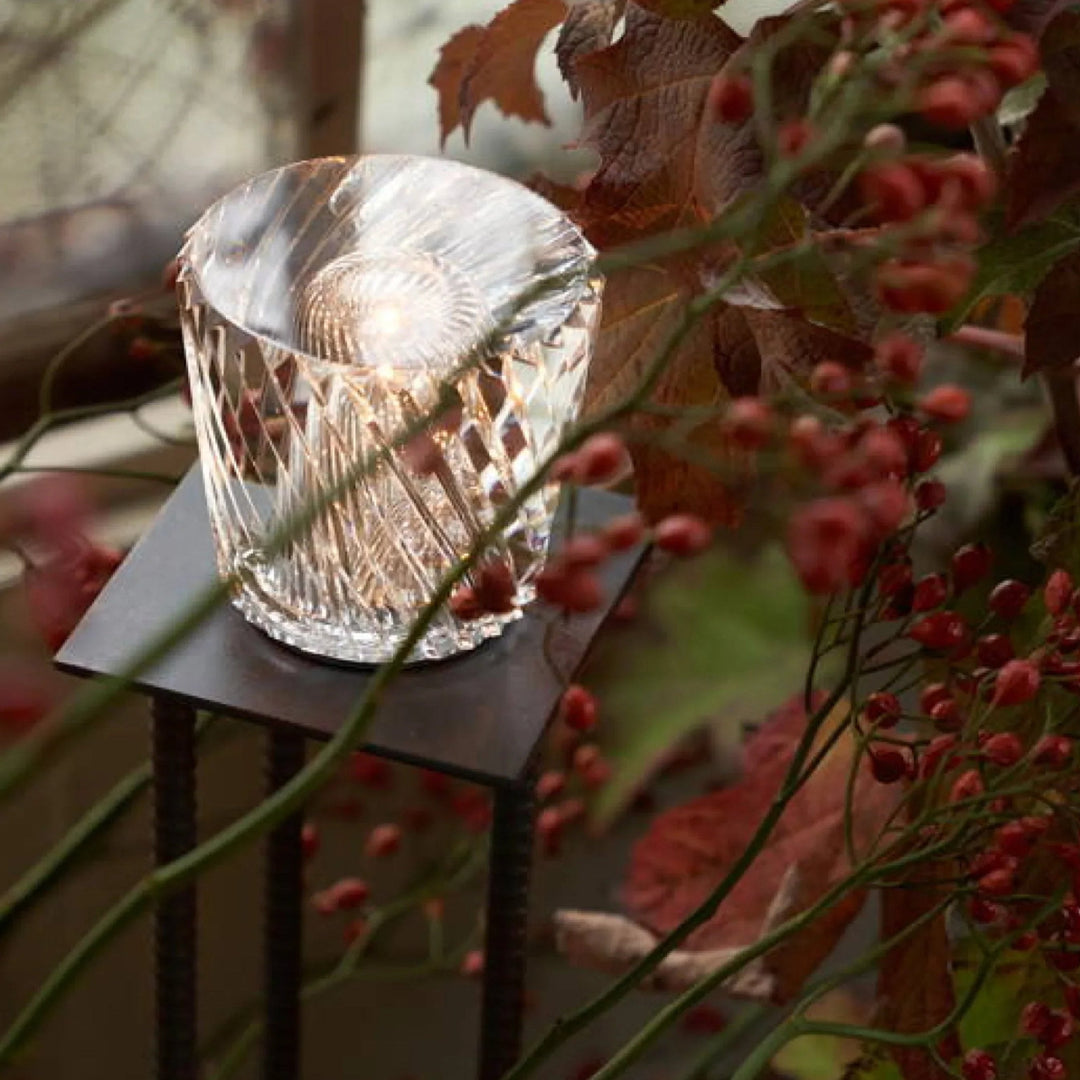 Gold transparent crystal table lamp, another view, on a small dark metal stand outdoors.