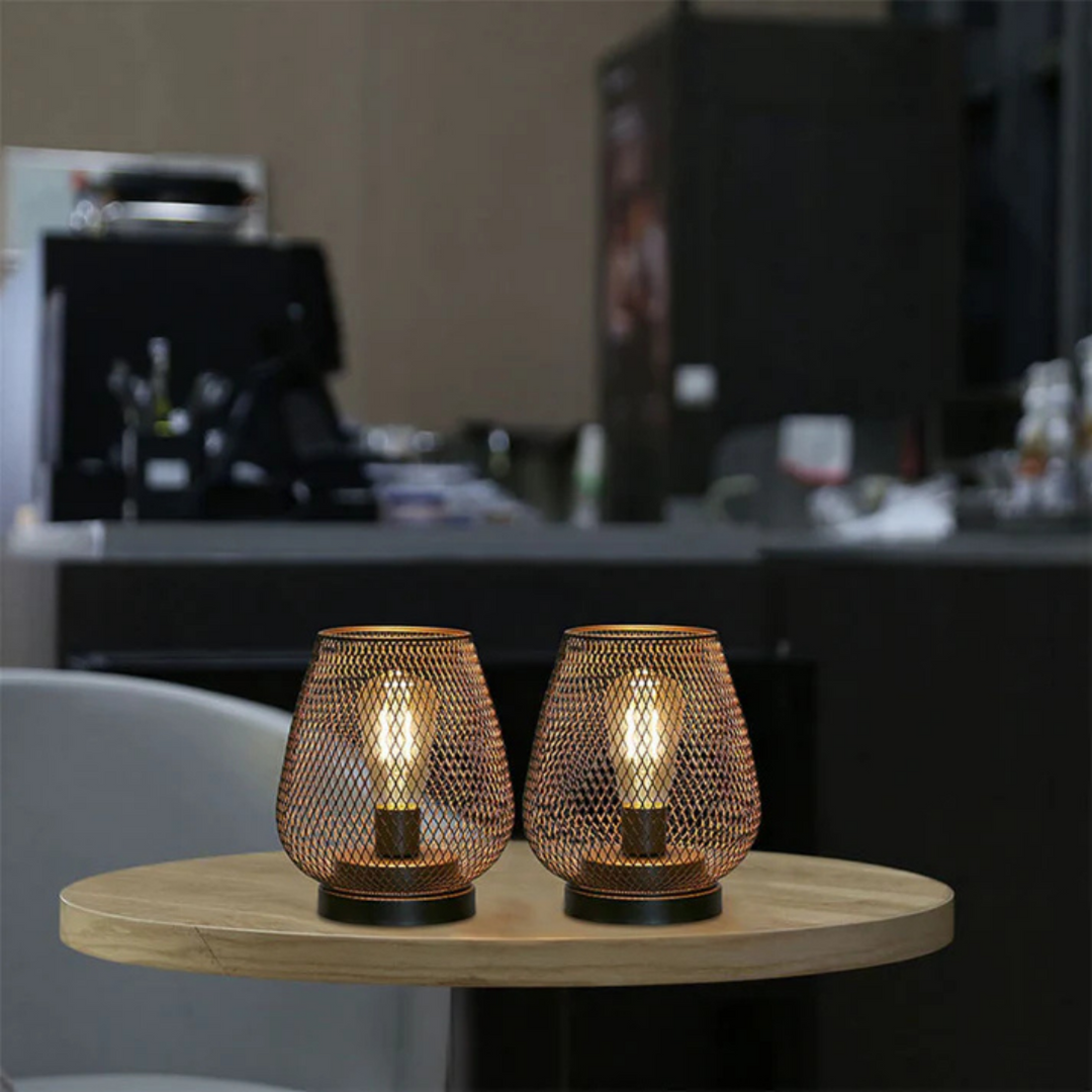 Pair of lit mesh lanterns on a round wooden table in a softly blurred cafe-style interior. 3