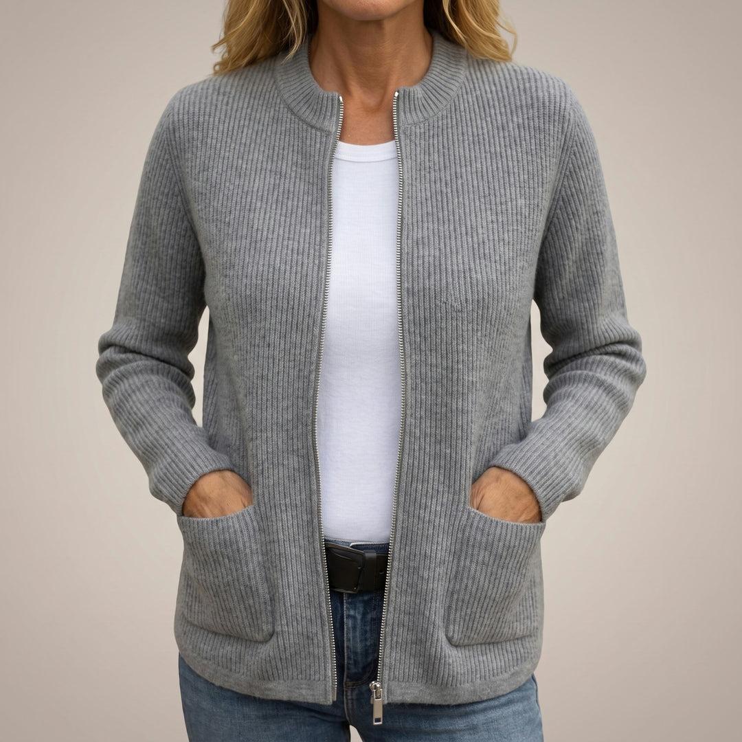 Woman wearing the ribbed zip-up cardigan in gray, unzipped over a white tee and jeans, hands tucked in the deep front pockets. 1