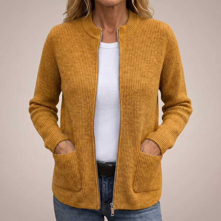 Woman wearing the ribbed zip-up cardigan in mustard yellow, unzipped over a white tee and jeans, hands in the front pockets. 3