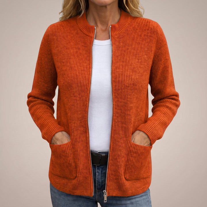Woman wearing the ribbed zip-up cardigan in burnt orange, open over a white tee and jeans, hands in the deep pockets. 4