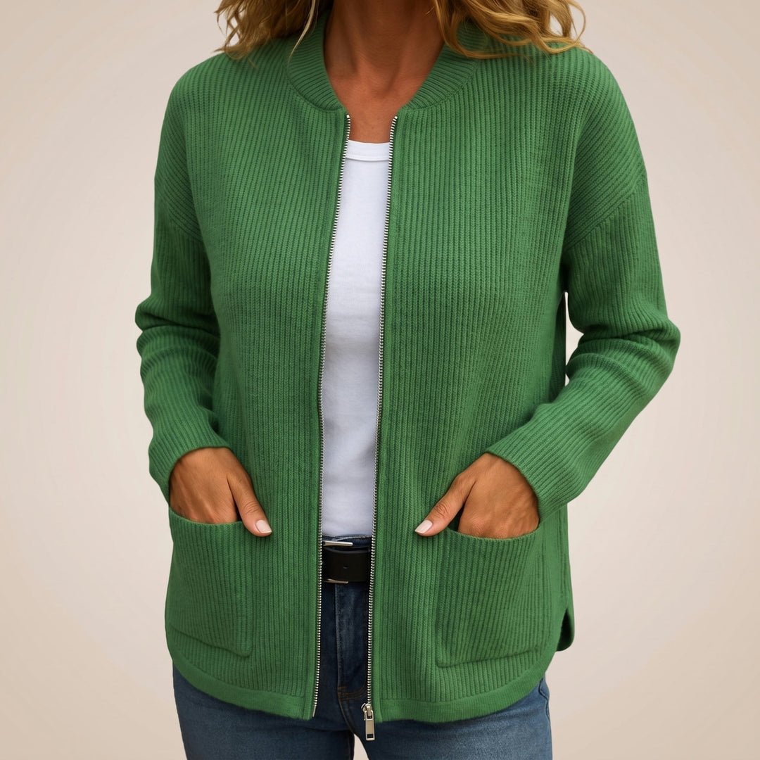 Woman wearing the ribbed zip-up cardigan in green, open over a white tee and jeans, hands in the pockets, with a small side slit. 6