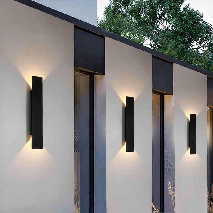Three black wall lights along a gray exterior wall glowing softly up and down.