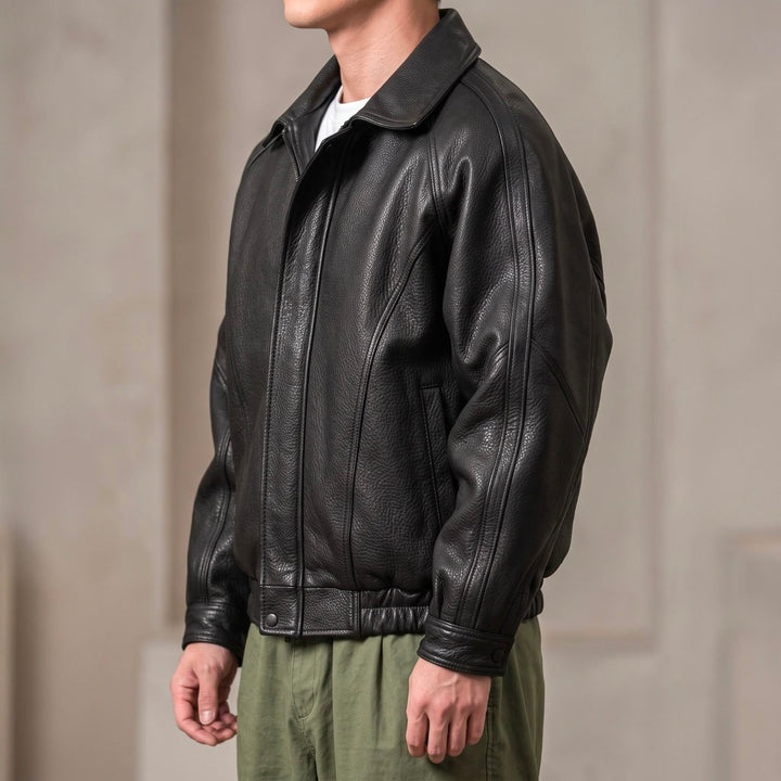 Side view of the black jacket on a model, showing the folded collar, seamed raglan sleeve, snap cuff and elastic hem.