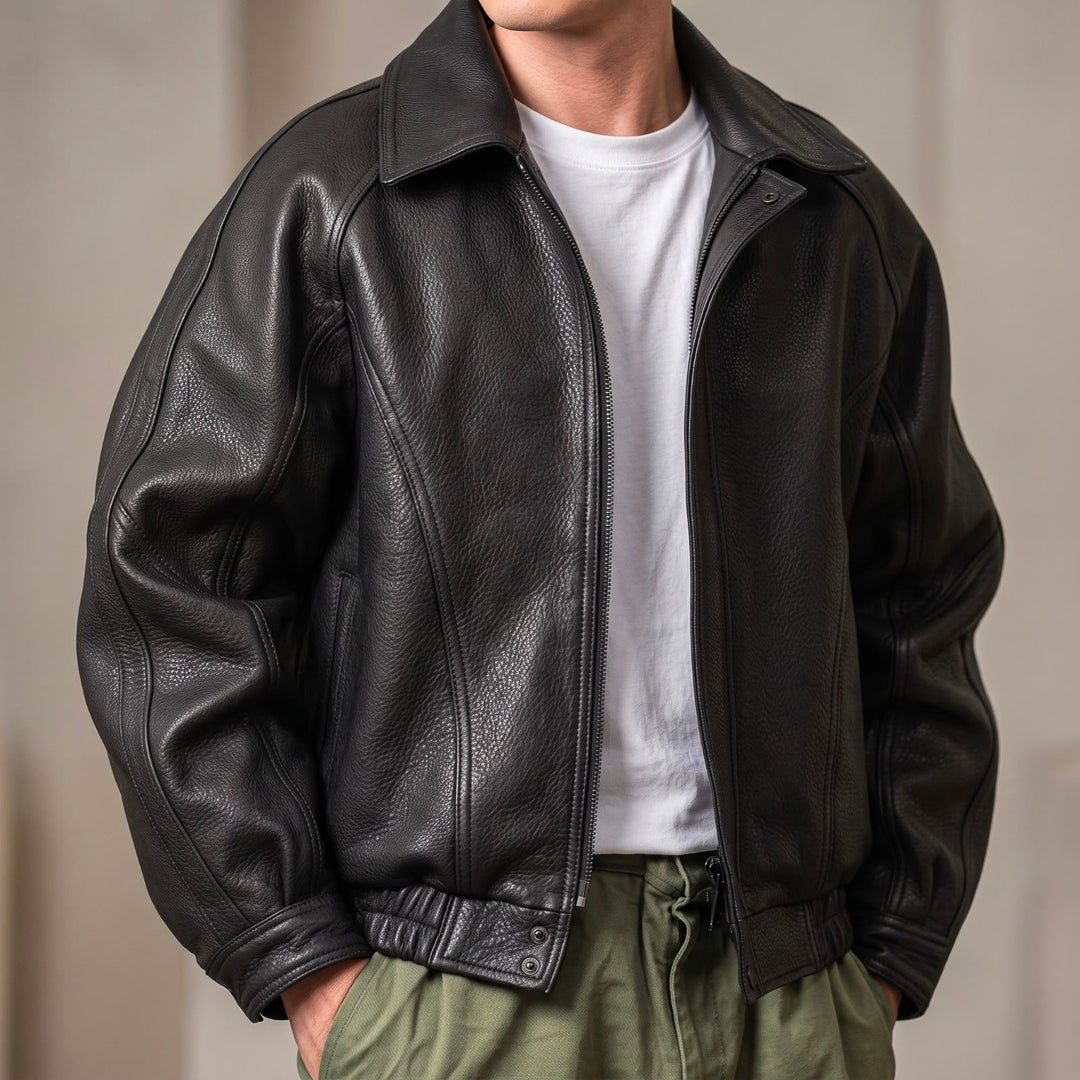 Front view of a model wearing the black grained leather jacket unzipped over a white tee and olive pants, hands in pockets. 1