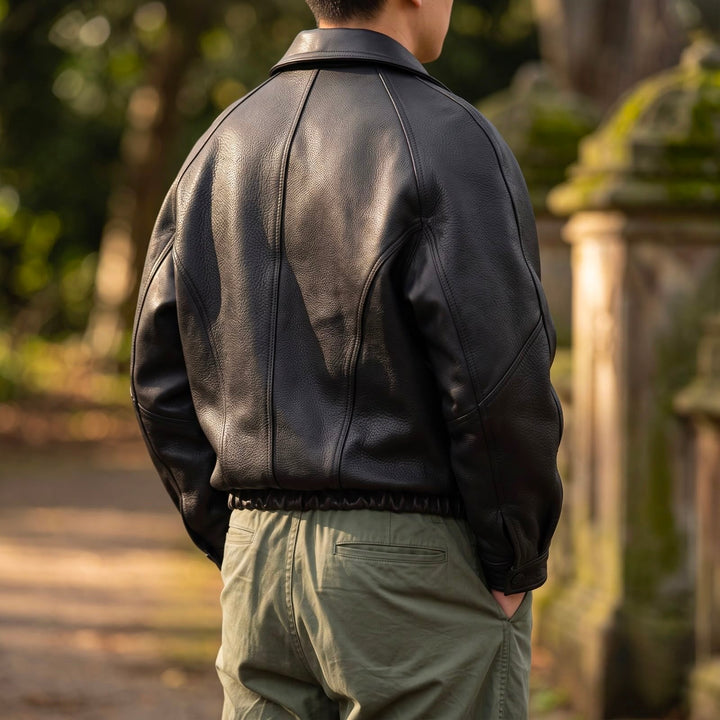 Back view of the black leather jacket worn outdoors with olive pants, showing the paneled back seams and elastic waistband. 3