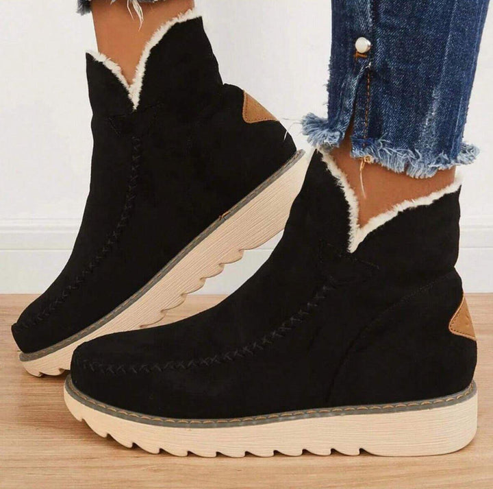 Black slip-on ankle boots with white fleece trim and cream ridged soles, side view.