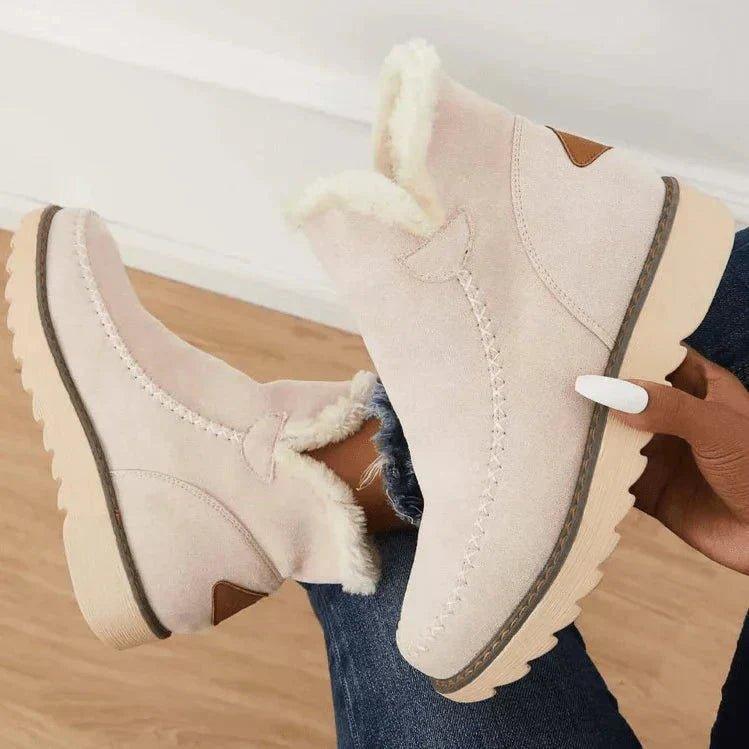 Beige fleece-lined slip-on boots with a stitched toe, brown heel patch and chunky ridged sole.