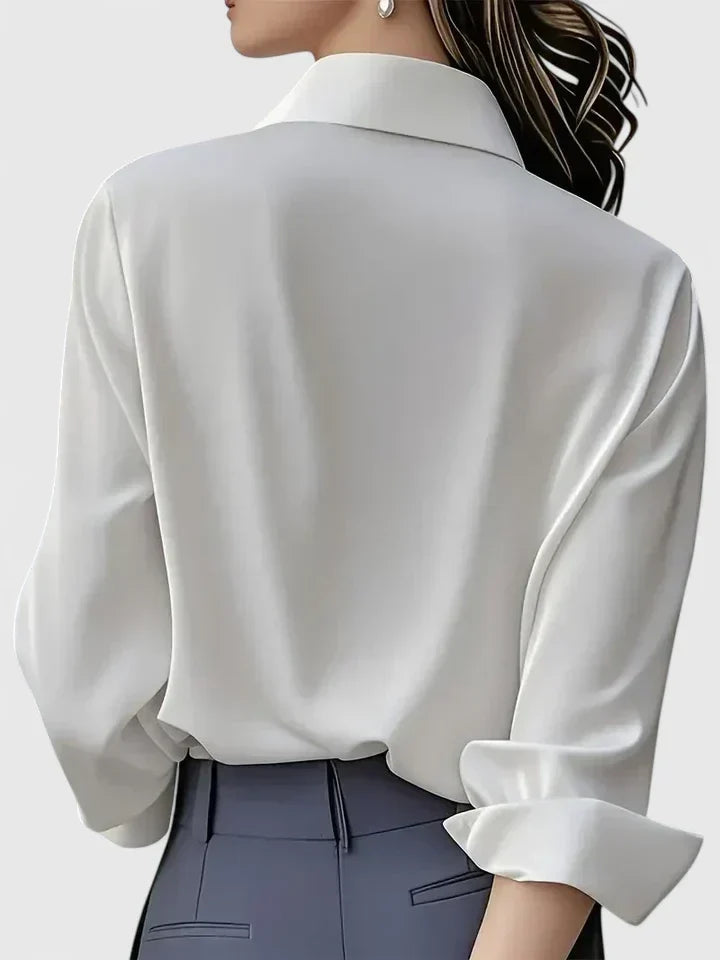 Back view of the white blouse on a model with gray trousers, showing the collar and rolled cuff.