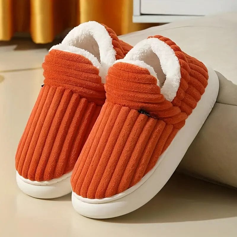 Pair of orange ribbed slippers with soft white fleece lining and thick white soles, resting on a floor in a cozy room. 22
