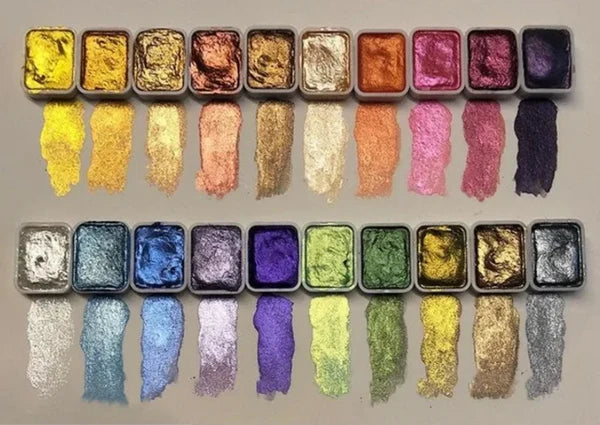 Top-down view of twenty shimmering paint pans in two rows, each with a brush swatch of its color beneath.