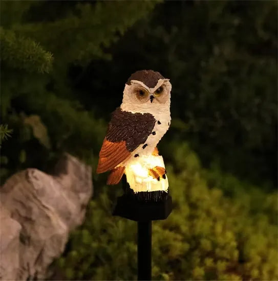 Brown-and-white owl light with orange-tinted wings lit at night beside a garden rock 7