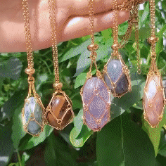 Another view of several gold cage necklaces with different stones hanging from a hand in front of green leaves. 4