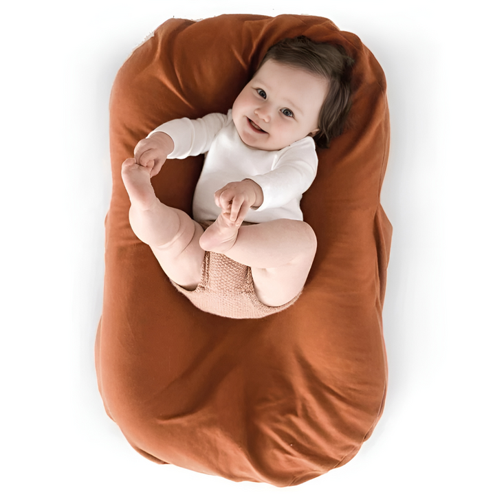 Smiling baby holds its feet while lying in a rust-orange lounger, seen from above 6