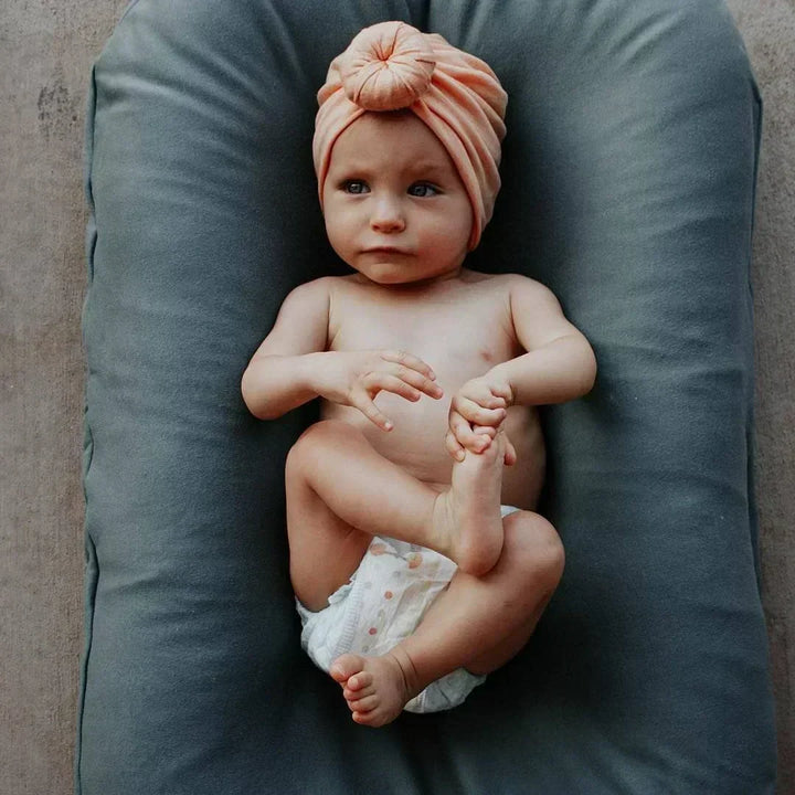 Baby in a peach knotted turban and diaper lying on a gray-green lounger 3
