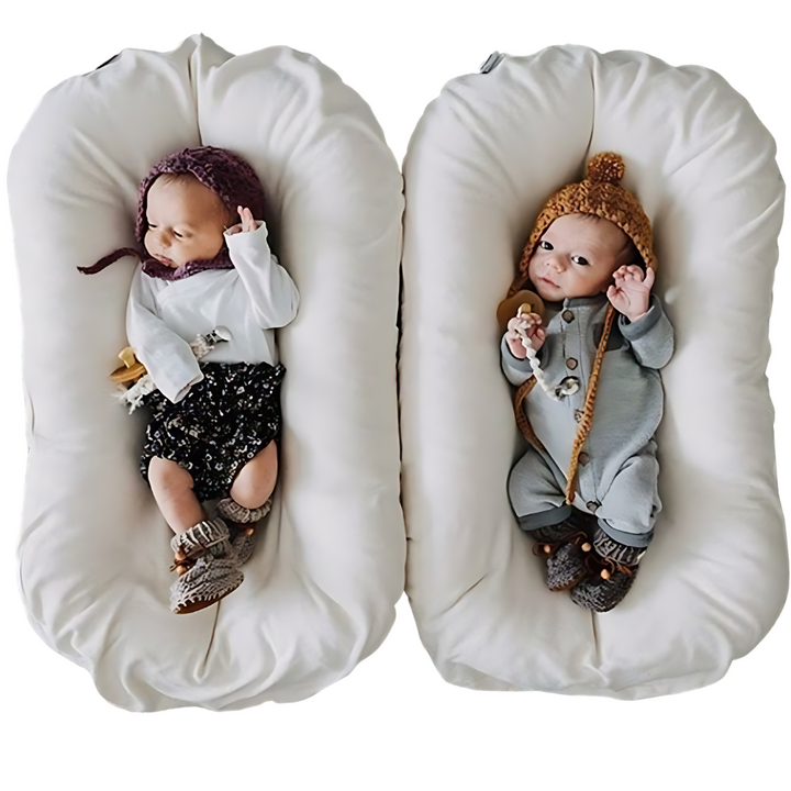 Two newborns in knit hats lie side by side in two cream loungers 5