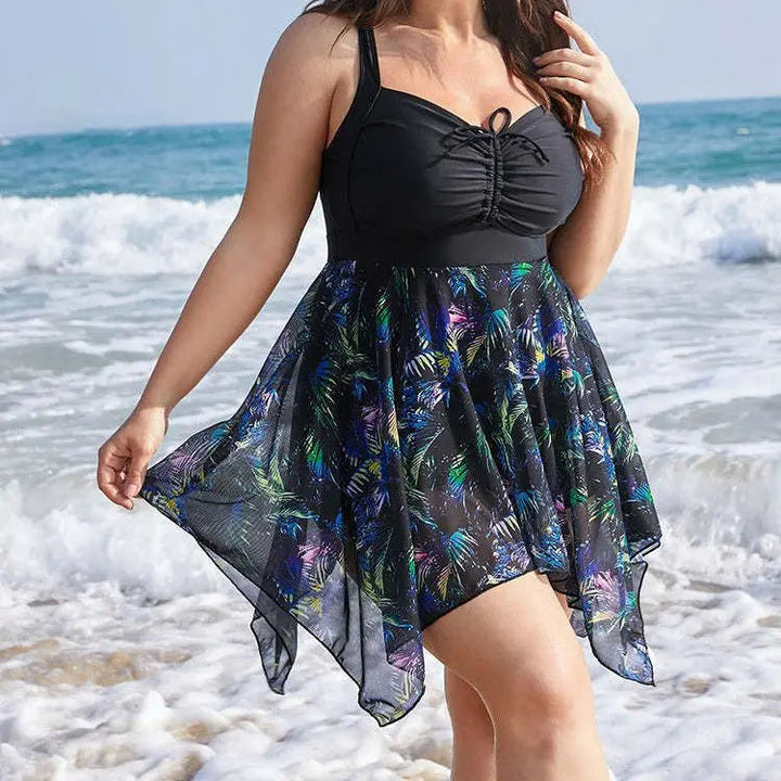 Frau im schwarzen Badeanzug mit buntem Rock am Strand vor Wellen im Hintergrund.