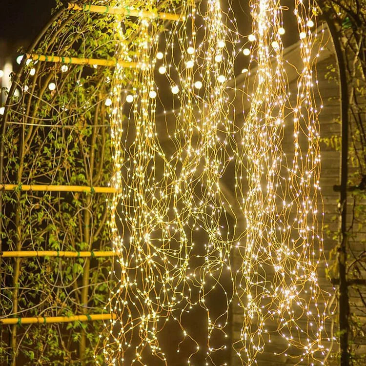 Cascading warm-white string lights hanging from a bamboo trellis with climbing greenery.