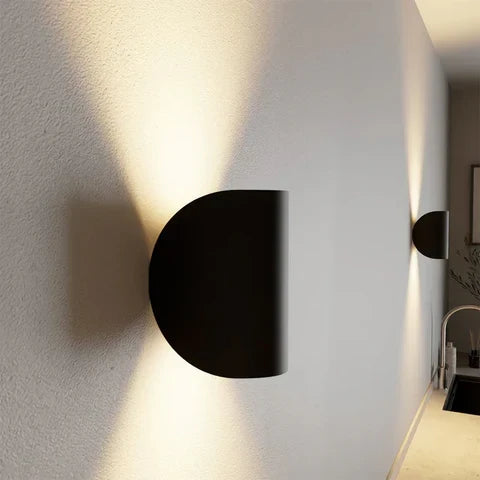 Side view of a black metal wall light on a textured wall, showing its depth with light fanning above and below.