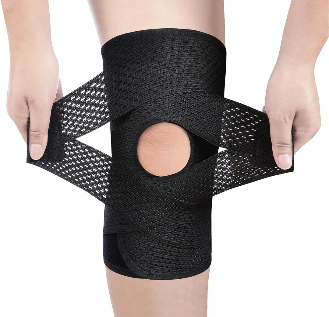 Both hands pulling apart the crossed black mesh straps of a knee wrap, showing the open kneecap hole on a white background. 9