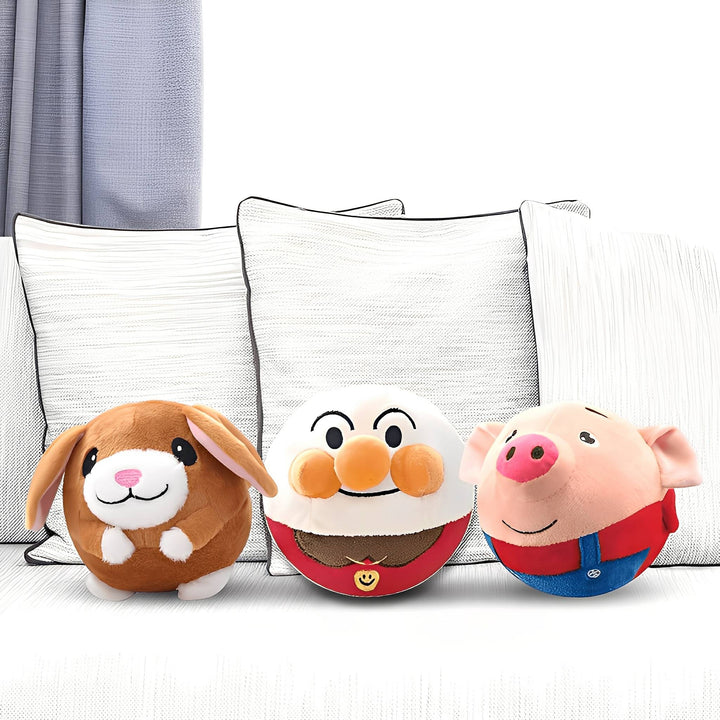Three round plush ball toys, a brown bunny, a smiling white character and a pink pig, lined up on a sofa.