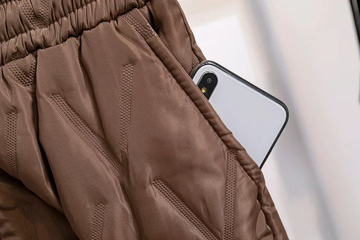Braune Steppjacke mit Smartphone in der Tasche, modische Winterbekleidung, isoliert.