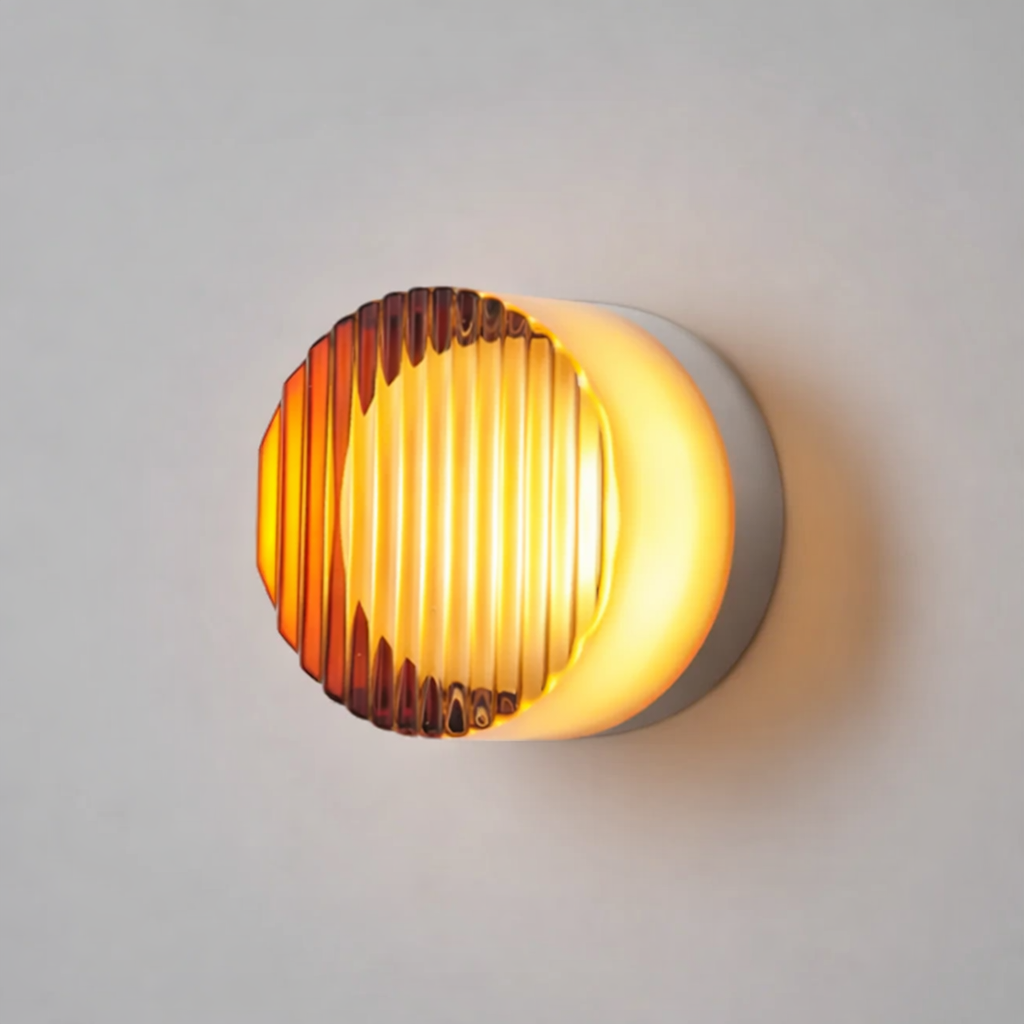Wall lamp with vertical ribbed amber glass front and a white round base, glowing with warm orange light. 32