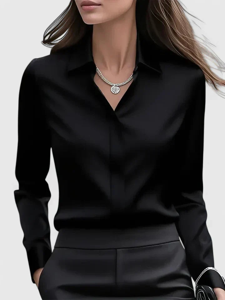 Front view of the black satin blouse worn open at the neck with a chain necklace and black trousers.