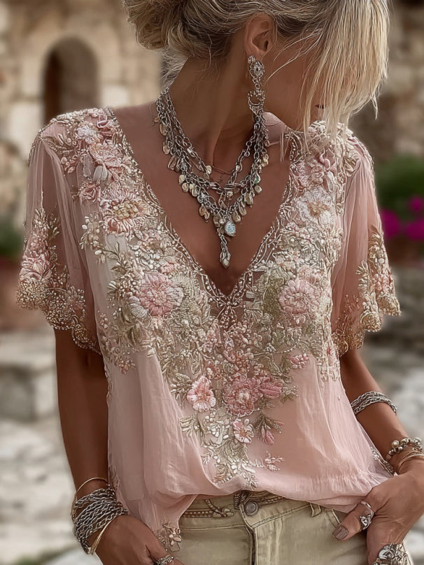 Model in a pink sheer blouse with embroidered flowers, layered silver necklaces and stone background, tall crop 1
