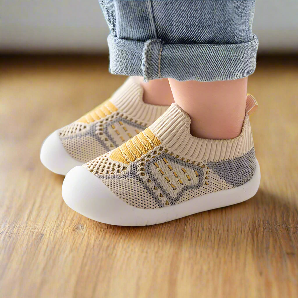 Beige and gray knit slip-on baby shoes with yellow stripes and white rubber soles, another view.