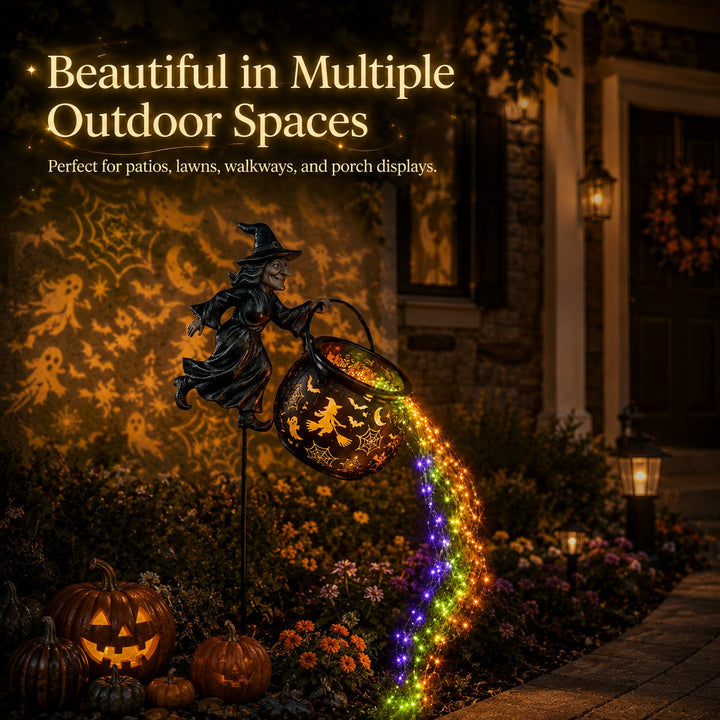 Another view of the witch cauldron light in a front-porch garden bed with carved pumpkins, a wreath, lanterns and projected patterns on the wall.