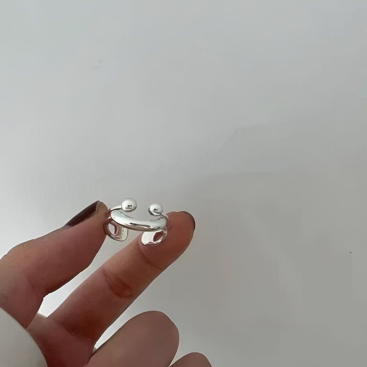 Ring held between two fingertips against a plain light wall, showing the cut-out openings on both sides of the band. 4
