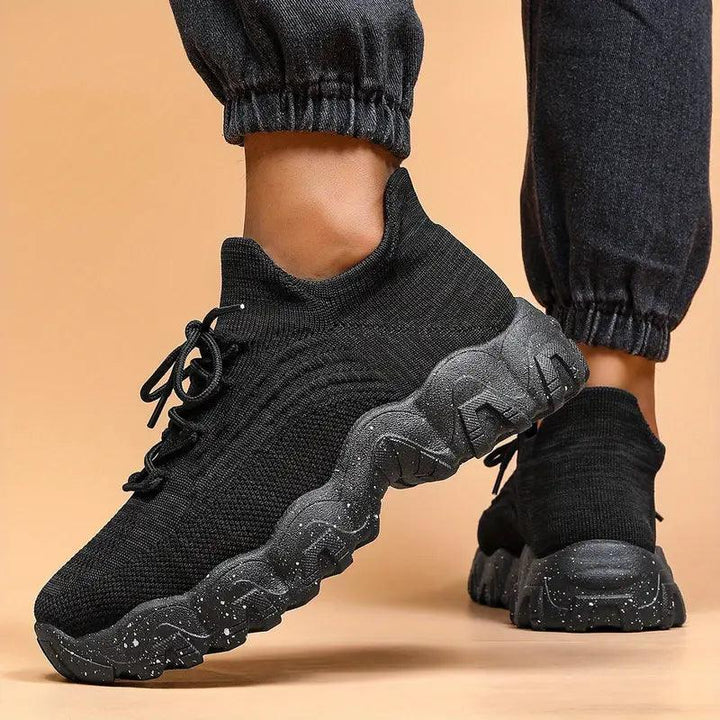 Another view of black knit sneakers with chunky speckled soles and gray joggers.