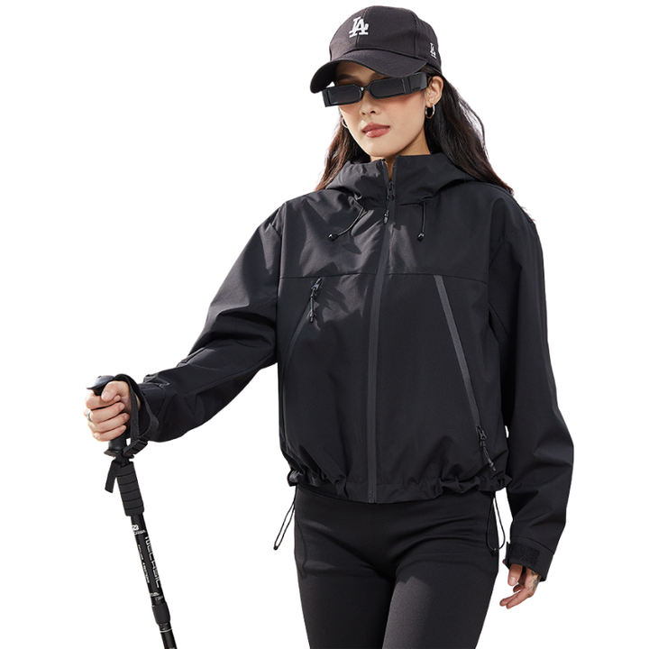 Black hooded jacket with tonal zips worn by a model holding a trekking pole, hem drawstring gathered. 14