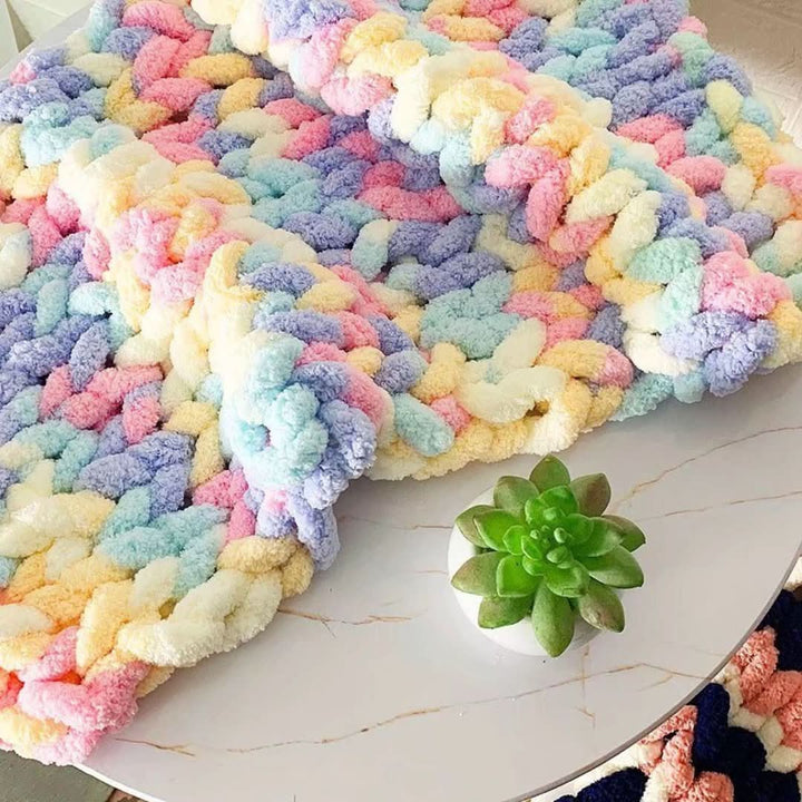 Chunky knit yarn in pastel pink, blue, lavender and yellow, draped over a marble-look table beside a small succulent.