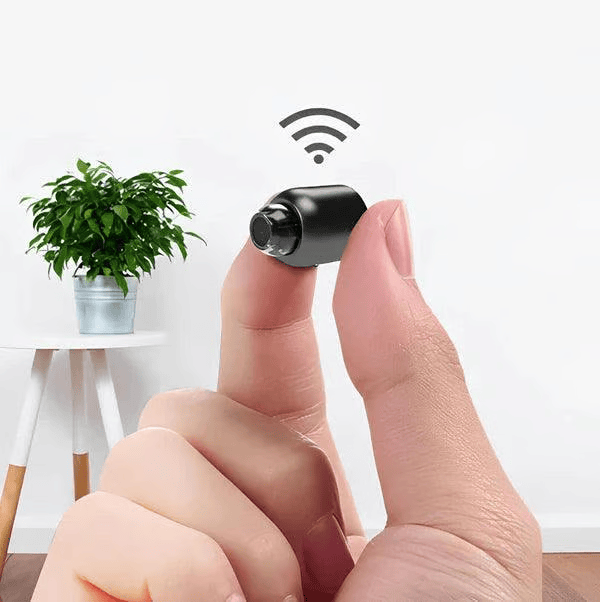 Black mini WiFi security camera detail held between fingertips