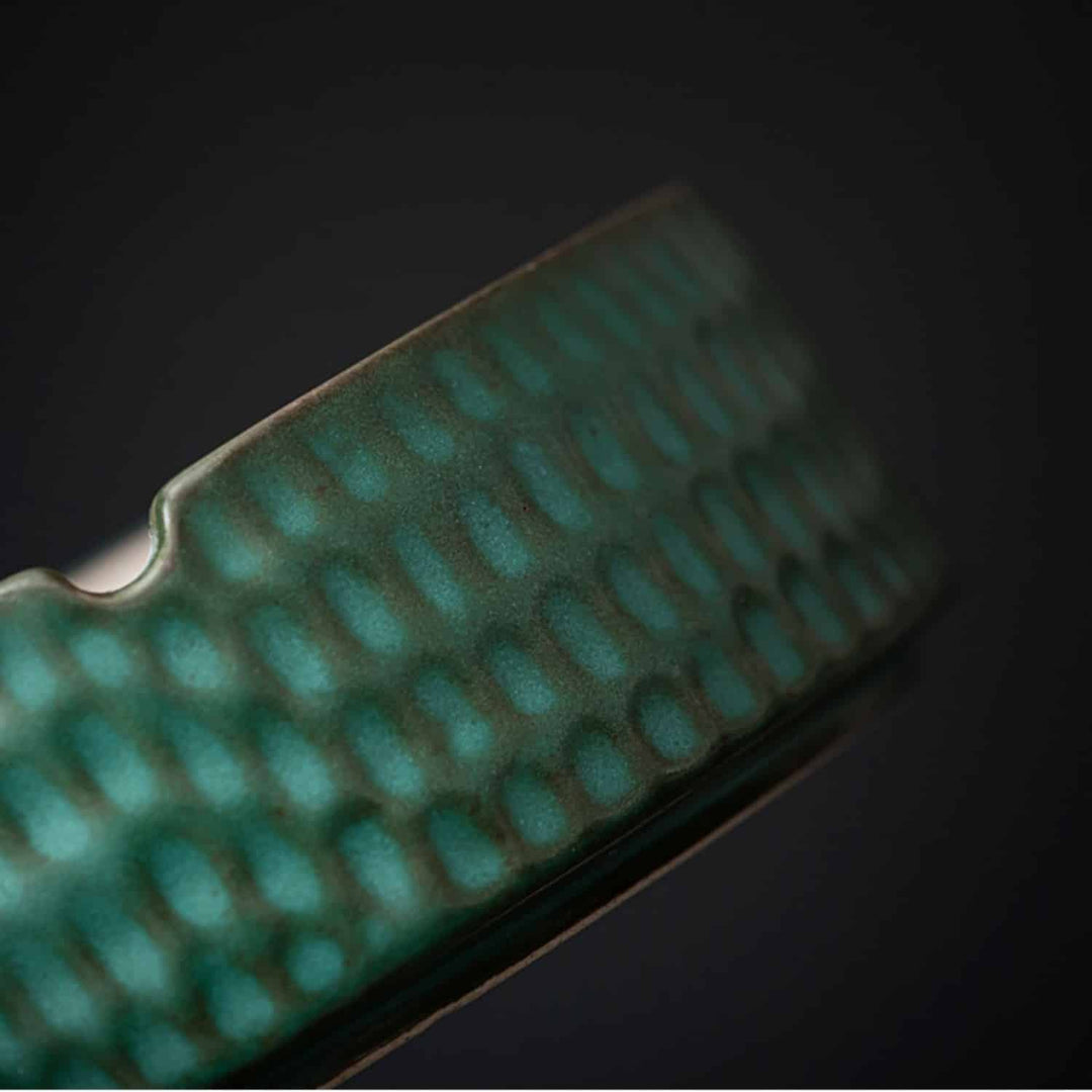 Green glazed ceramic ashtray detail showing the hammered outer wall and a cigarette notch.