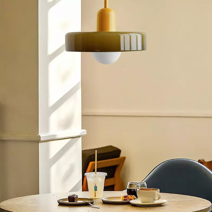 Olive glass pendant with a yellow cap hanging above a caf\u00e9 table with coffee and a pastry 16