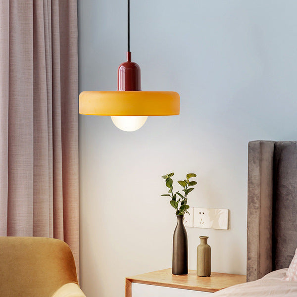 Amber glass pendant with a deep red cap hangs beside a bedside table with vases and a pink curtain 21