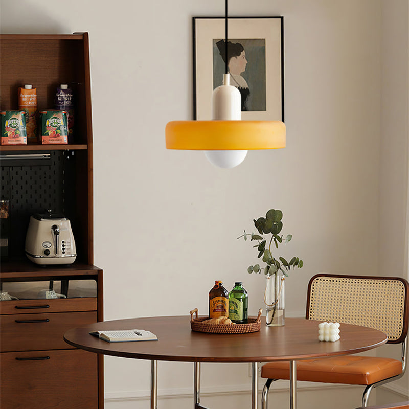 Amber pendant hanging over a round wooden dining table, with a shelving unit and framed portrait behind 30