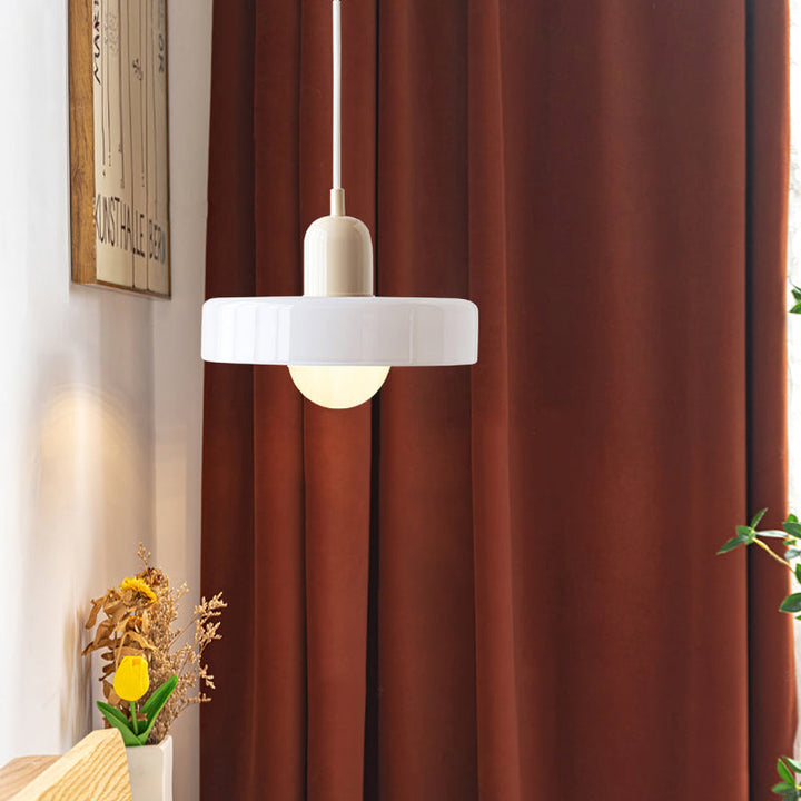 White disc pendant lamp with a cream cap hanging in front of a rust-colored curtain beside dried flowers 46