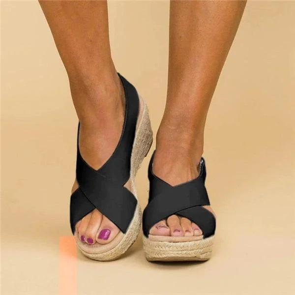 Straight-on front view of black crisscross wedge sandals with open toe and braided jute platform, worn on feet 9