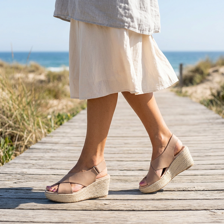 Woman in a linen skirt walking along a beach boardwalk in tan crossband wedge sandals 1