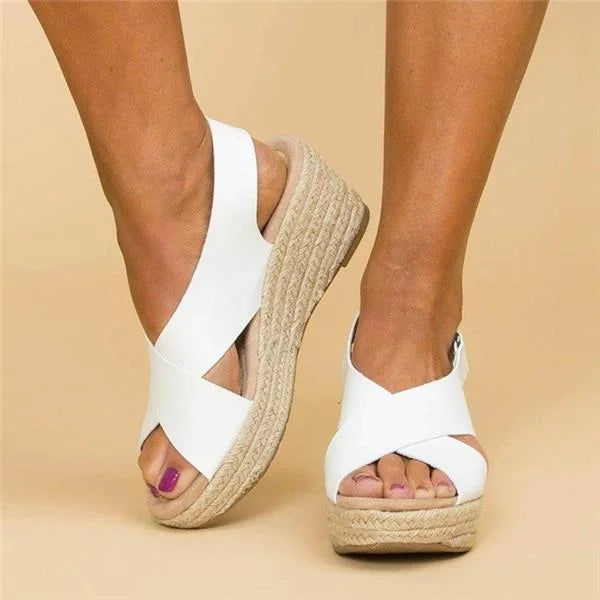 White crisscross wedge sandals worn on feet, front and side angle, with woven jute wedge 11