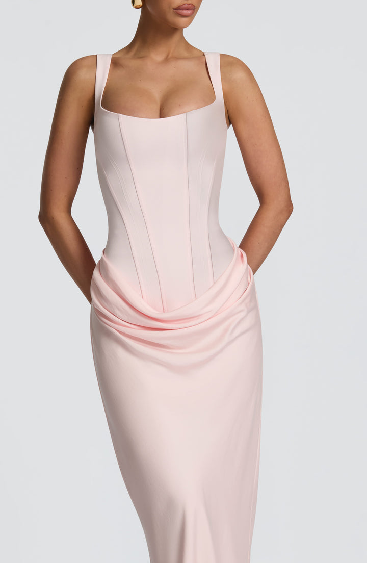 Close-up of the pale pink corset bodice with seam detailing, wide straps and draped hip panel, hands tucked behind the back. 21