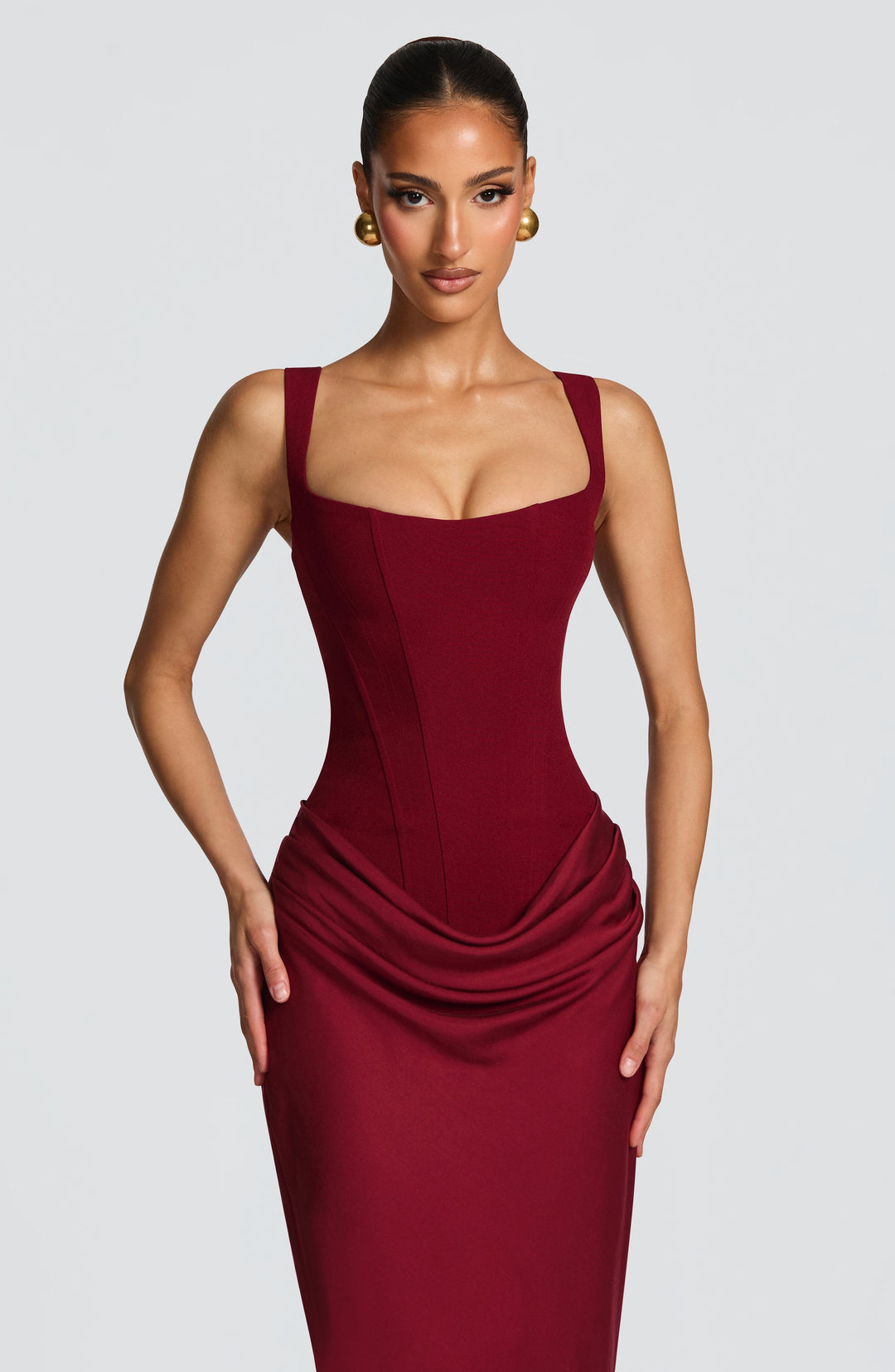 Upper-body close-up in burgundy, showing the square neckline, wide straps, boned corset seams and start of the draped hip. 26