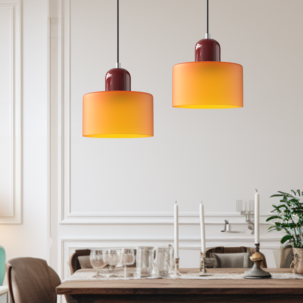 Pair of orange glass pendant lights with burgundy caps hanging over a dining table set with candles and glassware. 2