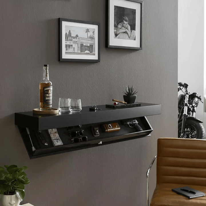 Black floating shelf mounted on a gray wall above a leather chair, with drinks on top and the compartment open showing cash, sunglasses and a handgun. 4