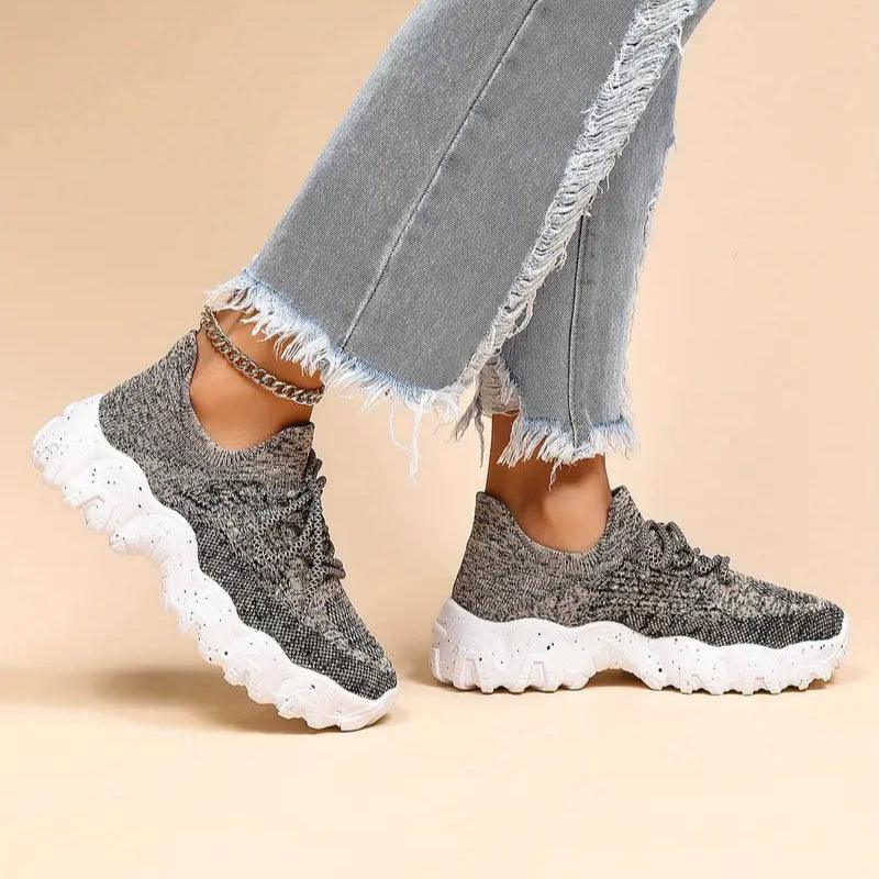 Model walking in gray knit sneakers with chunky white speckled soles, wearing distressed light jeans and a gold ankle chain. 39